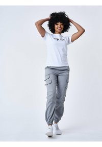 Witte t-shirt met zwarte bedrukking, gecombineerd met grijze cargobroeken met zijzakken en elastische boorden. Gestyled met witte sneakers.