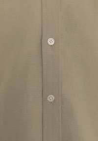 En tan knapp-up skjorta i mjukt tyg, med en rak knappslå som har två klara knappar och kontrasterande sömmar längs kanterna.