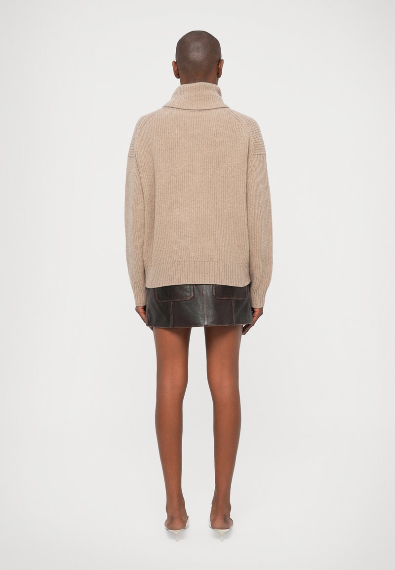 Beige stickad tröja med hög krage, ribbad textur och sjunkna axlar, i kombination med en mörkbrun läder minikjol.