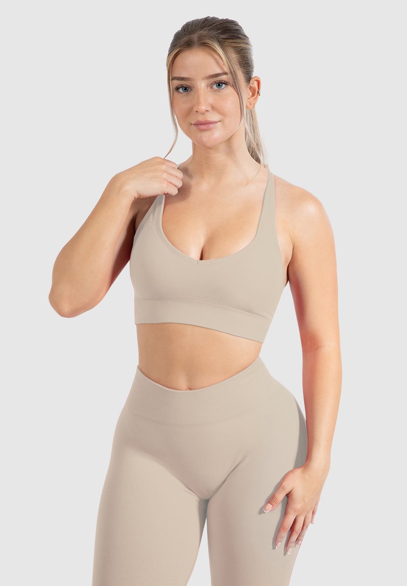 Sujetador deportivo beige con tirantes anchos y escote redondeado, combinado con leggings de talle alto en el mismo color. Tela suave y elástica.