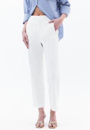 White tailored trousers with a slim fit, high waist, and side pockets. Smooth fabric and cropped length. Paired with a blue striped shirt.