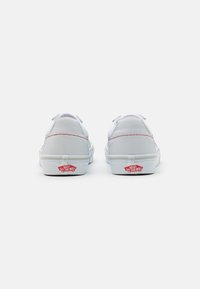 Sneakers bianchi in tela con un design a basso profilo, accentuati da dettagli in cucitura rossa e un logo rosso "Vans Off The Wall" sulla parte posteriore.