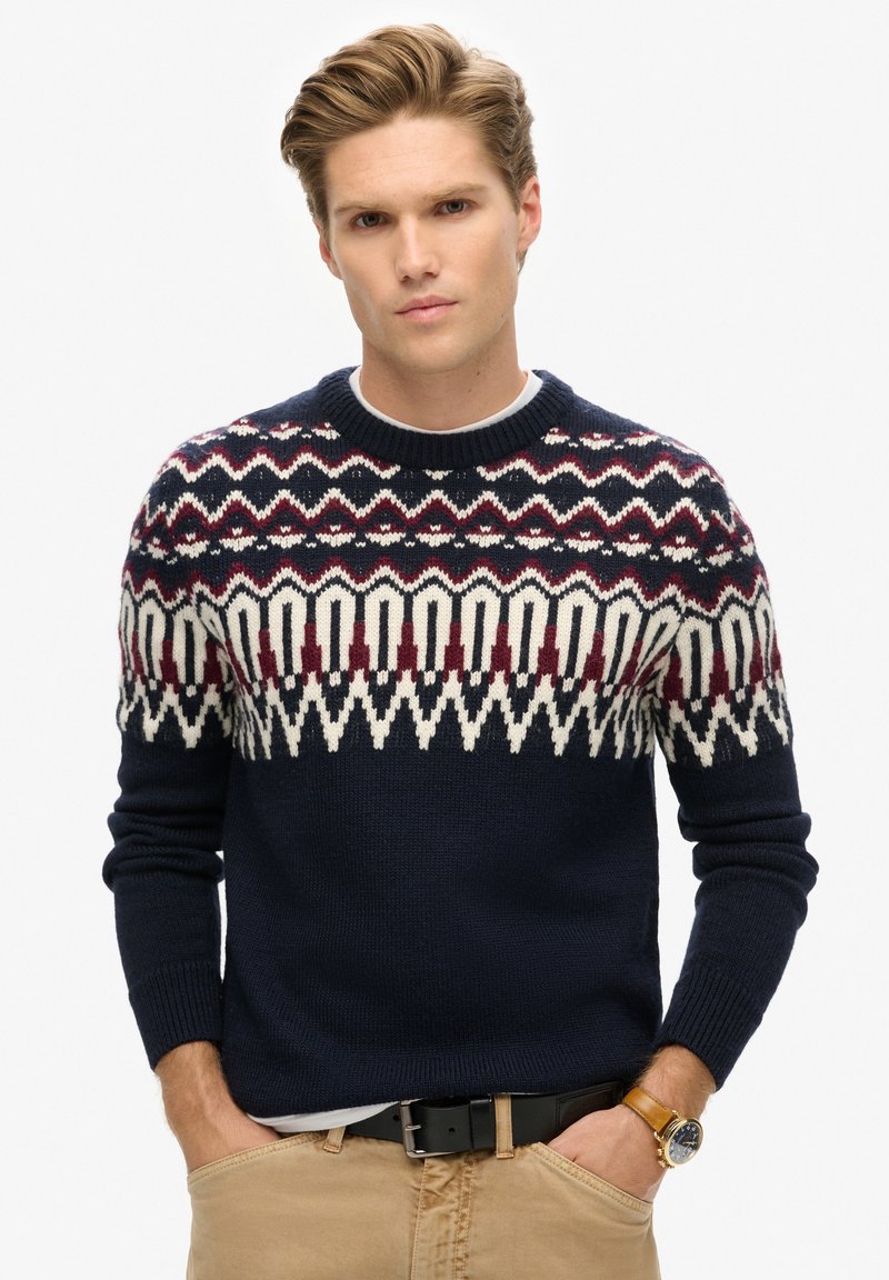 Marineblauer Pullover mit einem geometrischen Fair-Isle-Muster in Creme und Burgunderrot. Strickmaterial, Rundhalsausschnitt, figurbetonter Schnitt, lange Ärmel.