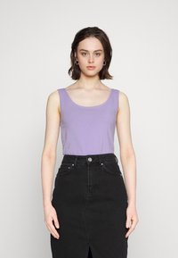 Top de tanque ajustado em lilás claro, com decote redondo, combinado com uma saia de ganga preta de cintura alta com uma fenda frontal e botão de metal.