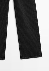 Black denim trousers with a pinstripe pattern, wide-leg cut, and raw hems, featuring a smooth texture and subtle stitching details.