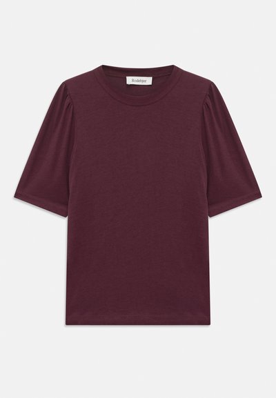 Camiseta corta de manga en burdeos con cuello redondo, textura suave y detalle fruncido en los hombros. Fabricada con material ligero.