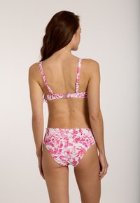 Blumiges Bikini-Set in Weiß mit pinken Blumen. Verfügt über verstellbare Träger und einen Hakenverschluss. Mittelhoher Slip mit hoher Beinausschnitt.