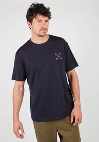 T-shirt en coton bleu marine avec des manches courtes et un col rond, présentant un petit motif géométrique coloré sur le côté gauche de la poitrine.