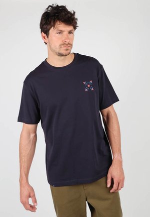 T-shirt en coton bleu marine avec des manches courtes et un col rond, présentant un petit motif géométrique coloré sur le côté gauche de la poitrine.
