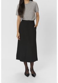 Pull court gris à manches courtes associé à une jupe noire longueur cheville avec une fente avant et des poches latérales, complété par des chaussures noires à bouts pointus.