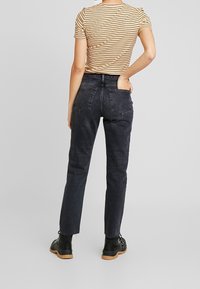 Jeans negros de talle alto con corte recto, que cuentan con bolsillos traseros y dobladillo deshilachado. Combinados con una blusa ajustada de rayas de manga corta.