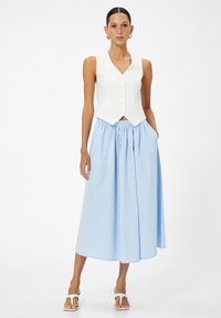 Chaleco blanco sin mangas con un dobladillo puntiagudo y cinco botones, combinado con una falda plisada de color azul claro que presenta bolsillos laterales.