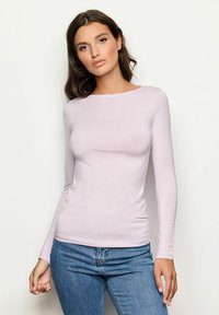 Langes, lilafarbendes, eng anliegendes Oberteil aus glattem Material, mit rundem Ausschnitt und schlankem Design, kombiniert mit blauen Jeans.