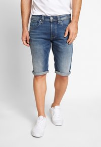 Denimshorts i ljus till medelblå tvätt, med uppvikta fållar, femfickorsdesign och synlig sömnad. Bärs med vita sneakers.