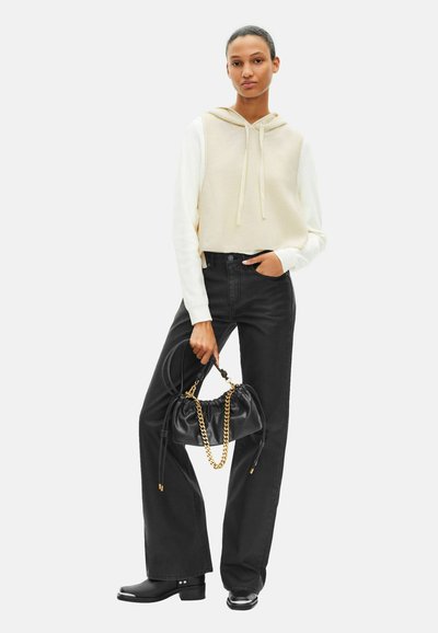 Cropped beige en crèmekleurige hoodie met trekkoorden, zwarte high-waist jeans, zwarte handtas met kettingaccent en zwarte enkellaarzen.