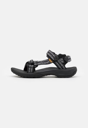 Sandalia deportiva Teva negra y gris con tiras ajustables y suela acolchada, diseñada para uso exterior y casual.