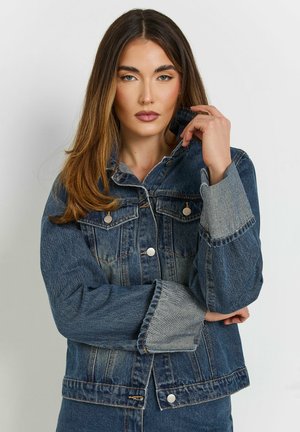 Giubbotto di jeans blu scuro con un design aderente, due tasche sul petto, bottoni argentati e polsini più chiari a contrasto. Tessuto morbido e strutturato.