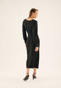 Black long-sleeve dress with a fitted bodice, ruched detailing at the waist, and a knee-length hem. Smooth fabric and round neckline.