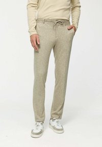 Beige textúrájú nadrág, állíthat�ó derékpánttal, diszkrét mintázattal. Fehér és szürke sportcipővel párosítva. Fitt szabású.