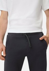 Zwarte joggingbroek met elastische tailleband en gestippelde trekkoord, voorzien van zijzakken en een soepele textuur, gecombineerd met een wit T-shirt.