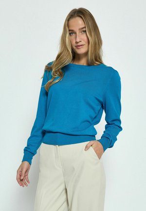 Blue knitted sweater with a round neckline and long sleeves, featuring ribbed cuffs and hem. Smooth texture, paired with beige pants.