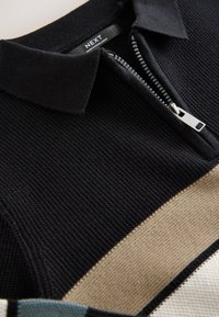 Sort strikket poloshirt med lynlås, der har en beige stribe og kontrasterende teksturer. Labelen viser "NEXT."