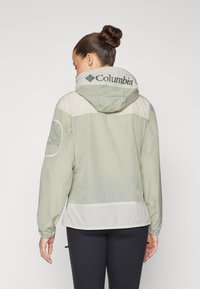 Letthvægts Columbia jakke i blød grøn og creme, med hætte, mesh-detaljer på ærmerne og logo på ryggen.