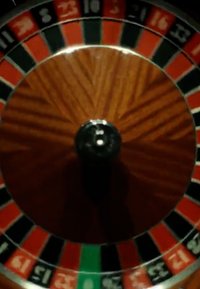 Rulettespillhjul som spinner med vekslende røde, svarte og grønne nummererte lommer på en trebase med en sentral svart spindel.