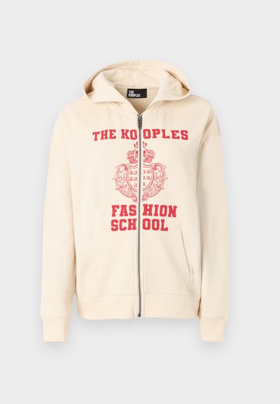 Μπεζ φούτερ με φερμουάρ και κόκκινο εκτυπωμένο κείμενο "THE KOOPLES FASHION SCHOOL" και σχέδιο κορώνας. Διαθέτει κουκούλα και δύο μπροστινές τσέπες.