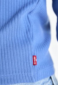 Kék bordázott kötött póló, a hemnél egy kis piros Levi's címkével. A szövet puha, látható textúrával és laza szabással rendelkezik.