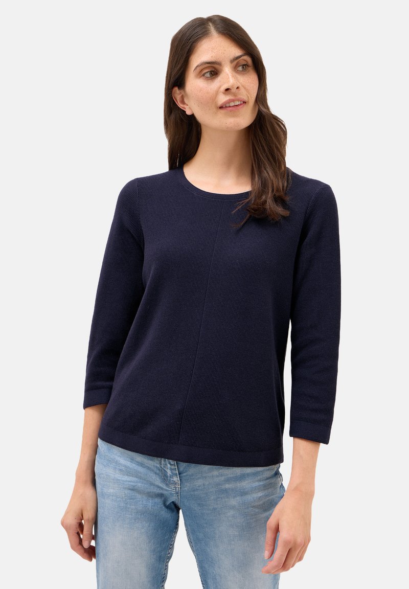 Mörkblå stickad tröja med trekvartslånga ärmar, rund hals och ett strukturerat mönster. Kombination med ljusblå jeans.