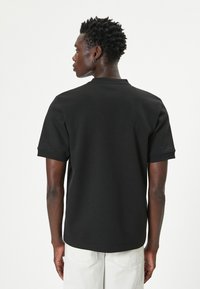 Sort kortærmet t-shirt med rund hals, glat bomuldsstof, afslappet pasform og foldede manchetter. Synlige sømdetaljer.