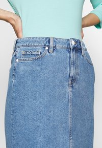 Džínová sukně s světle modrým odstínem, vysokým pasem, předními kapsami a jemnými švy. Tkanina má hladkou texturu.