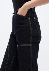 Σκούρα τζιν με ψηλή μέση, ραφές σε αντίθεση, πλαϊνές τσέπες και άνετη γραμμή. Ασημένιες λεπτομέρειες στις αγκράφες στη μέση.