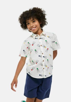 Chemise à manches courtes avec col, de couleur blanc cassé, ornée d'un motif de volants colorés ; boutons marron et coupe décontractée.