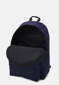 Námorně modrý batoh s černým interiérem, otevřená hlavní přihrádka, černá zipová síťovaná kapsa a vrchní uchopovací rukojeť na bílém pozadí.