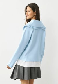 Jasnoniebieski sweter z dużym kołnierzem marynarskim, zdobiony niebieskimi paskami, zestawiony z białym warstwowym brzegiem i plisowaną ciemnoszarą spódnicą.