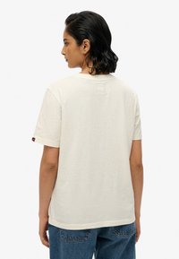 Crèmekleurig katoenen T-shirt met een klassieke ronde hals, korte mouwen en een klein label aan de linkermouw. Eenvoudig ontwerp zonder patronen.