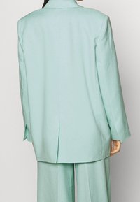 Blazer oversize verde menta con uno spacchetto sul retro e maniche ampie, abbinato a pantaloni coordinati, caratterizzati da una texture liscia.