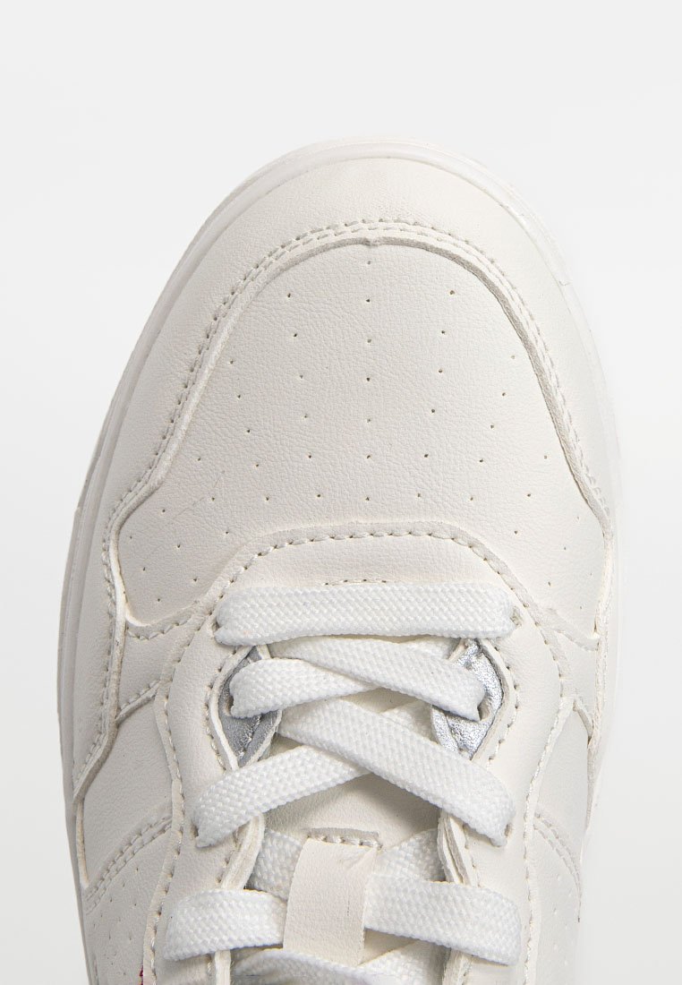 Sneaker en cuir blanc avec une boîte à orteils perforée, des lacets plats et un col rembourré. Design minimaliste avec des coutures discrètes et des accents argentés.