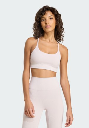 Γυναίκα με σγουρά μαλλιά που φοράει ροζ ριμπ αθλητικό σουτιέν και ψηλόμεσα κολάν μπροστά σε απλό φόντο.