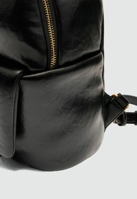 Zaino in pelle nera con finitura testurizzata, dotato di una cerniera dorata, tasca laterale e tracolla regolabile.