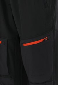 Schwarze Hosen mit kontrastierenden orangefarbenen Reißverschluss-Taschen, hergestellt aus einem strapazierfähigen Material mit glatter Textur und dezentem Branding.