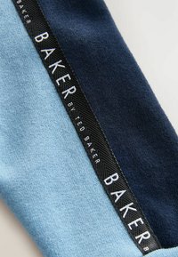 Bufanda de tejido de punto con secciones en azul claro y azul oscuro. Presenta una etiqueta texturizada negra con el texto "BAKER" en blanco.