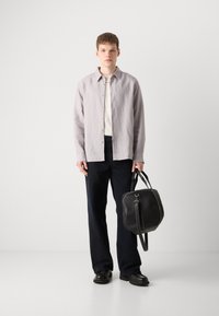 Lichtgrijze overhemd, off-white T-shirt, donkere broek en zwarte tas. Tas is textuur, met een handvat bovenop en een schouderband. Zwarte schoenen.
