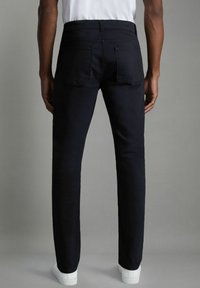 Donkerblauwe slim-fit denim jeans, met klassieke achterzakken en een nette afwerking. Gecombineerd met witte schoenen.