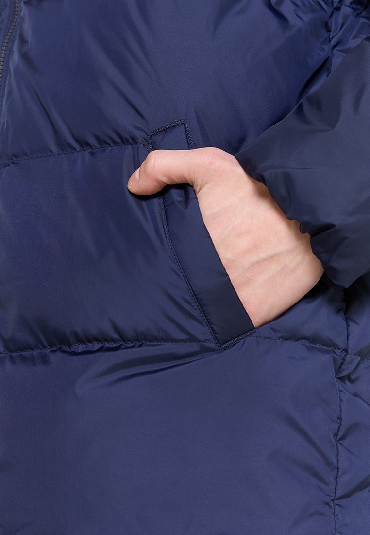 Doudoune bleu marine avec une poche visible sur le côté gauche. Le tissu est lisse et légèrement brillant, avec des sections matelassées pour l'isolation.