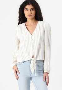 White tie-front blouse with vertical black stripes, v-neckline, button detailing, and long sleeves with gathered cuffs.