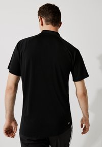 Černé polo tričko s krátkým rukávem, hladkým povrchem a klasickým límečkem, s prošitými akcenty a jemným logem na lemu.