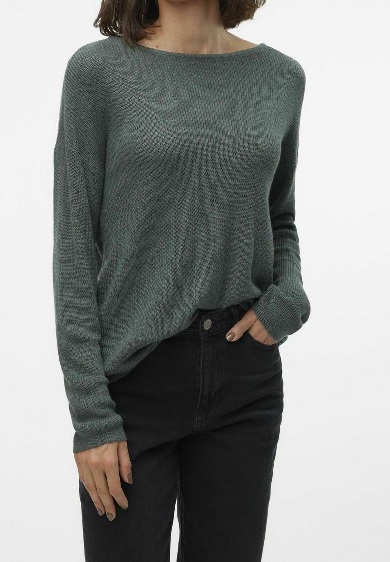 Leichter, gerippter Langarmpullover in dunklem Grün mit weitem Halsausschnitt und lässiger Passform. Getragen mit hochgeschnittenen schwarzen Jeans.